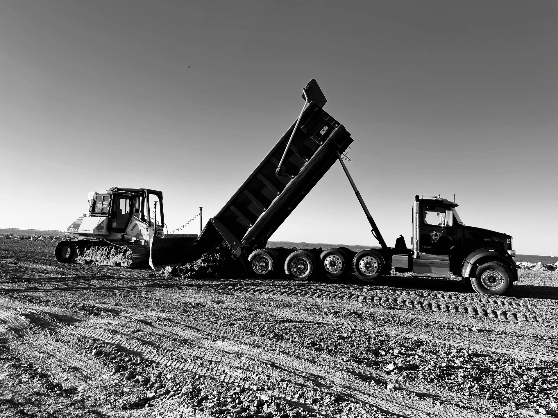 Dump truck raising its bed to unload soil as a bulldozer works behind it