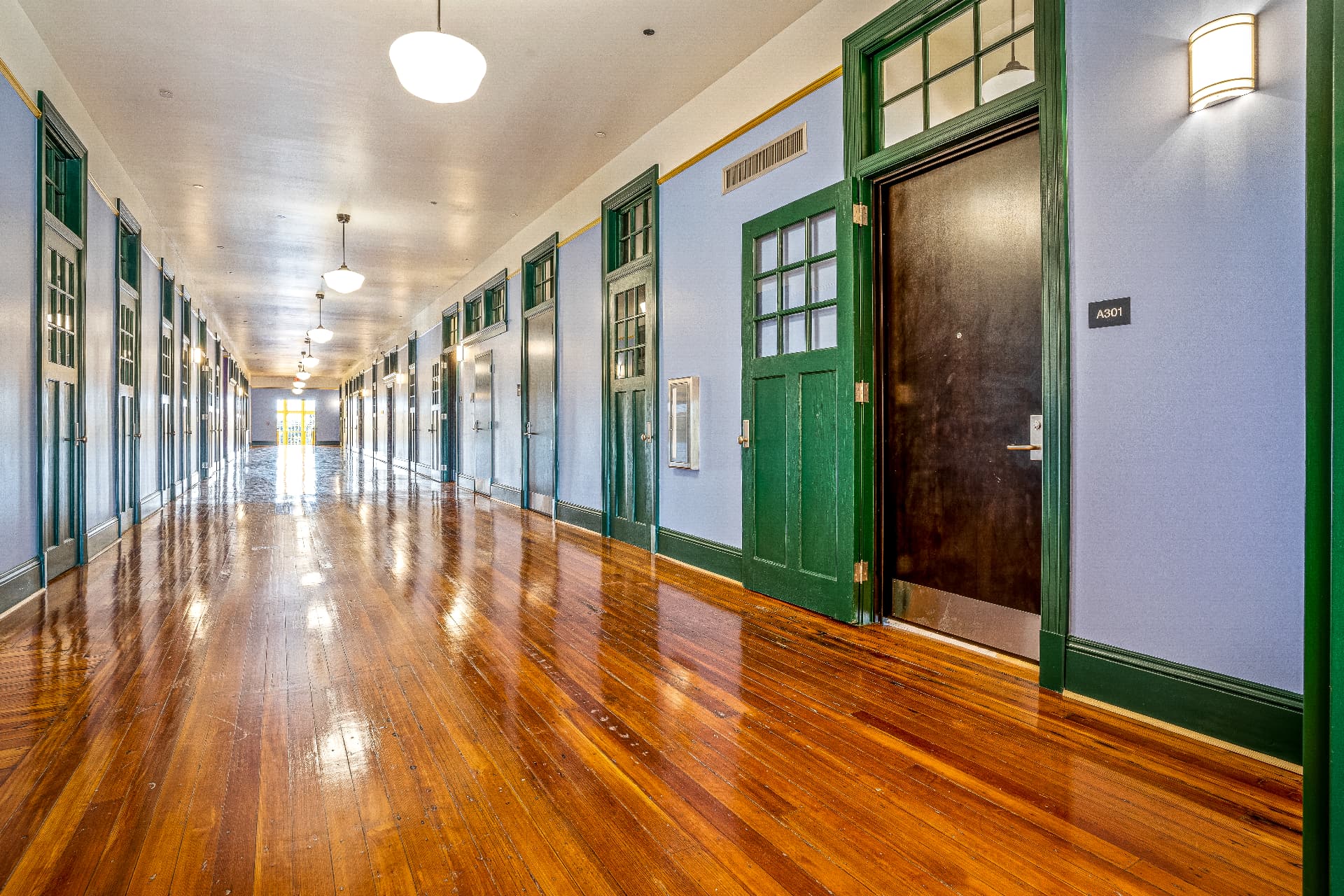 Restored school hallway with green-trimmed doors and polished wood floors