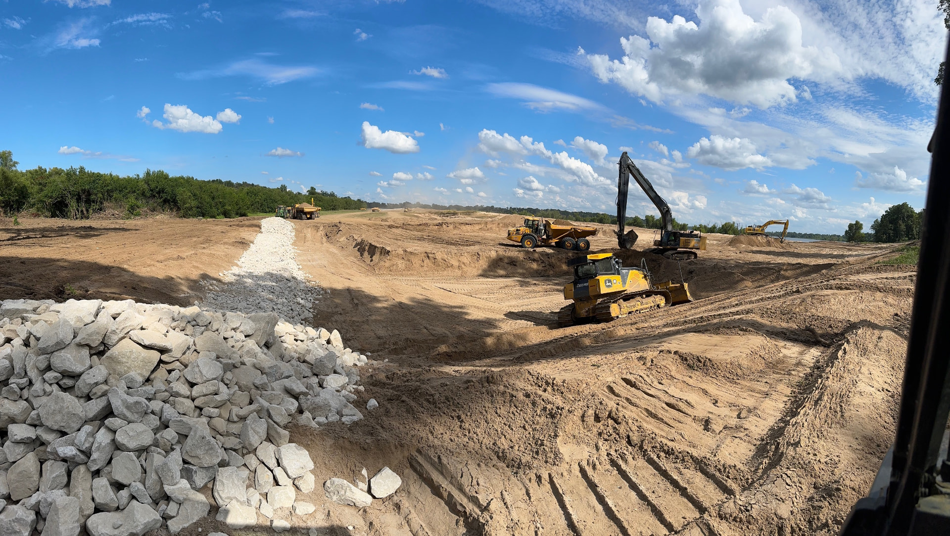Earthwork site with excavator, dozer, and haul trucks shaping a drainage channel
