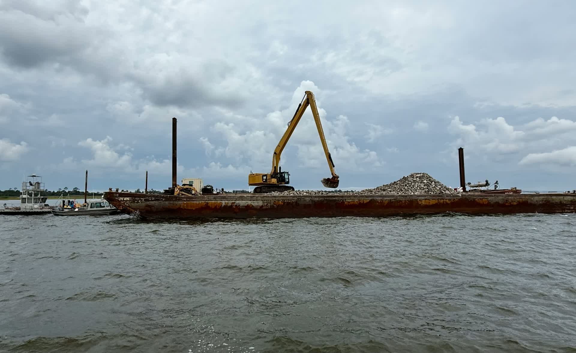 Long-reach excavator on a spud barge loading rock on open water